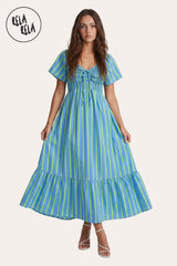 Front profile of the model in the Blue Stripe Maxi Dress, showcasing the flexible smocked waist and the fluid, tiered ruffle skirt.