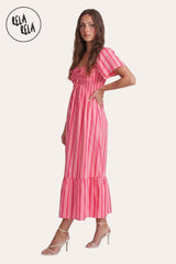Side profile of the model in the Pink Stripe Maxi Dress, showcasing the stretchy smocked bodice and the fluid, tiered ruffle hemline.