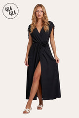 Front view of a model wearing the Black Flower Corsage Wrap Maxi Dress, showcasing the timeless noir drape and the sculptural 3D floral waist accent.