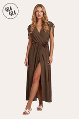 Front view of a model wearing the Chocolate Flower Corsage Wrap Maxi Dress, showcasing the rich cacao-hued drape and the tonal 3D floral waist accent.