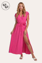 Front view of a model wearing the Hot Pink Flower Corsage Wrap Maxi Dress, highlighting the vibrant fuchsia drape and the sculptural 3D floral waist accent.
