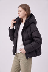 Angled model view of a black cropped puffer jacket worn open, showing the zip beneath the snap-button placket, padded hood and long sleeves.