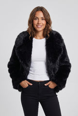 Open front model view of a black short faux fur jacket, showing the plush texture and oversized collar, styled with a white top and black trousers.