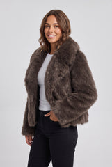 Angled front model view of a chocolate brown short faux fur jacket, showing the plush texture, oversized collar, long sleeves and short hem.