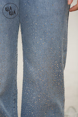 Close-up of rhinestone detailing on mid blue denim sparkle wide leg jeans.