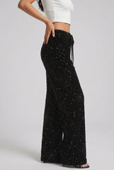 Side model view of black sequin trousers, showing the drawstring waistband, wide-leg shape and full-length hems.