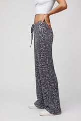 Side model view of grey sequin trousers, showing the drawstring waist, relaxed wide-leg shape and full-length hems.