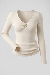 Flat product image of the cream ribbed V-neck top with decorative gold-tone buckle.