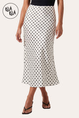 Front view of a model in Rela Rela’s White satin polka dot maxi skirt. Highlights the clean monochromatic palette and the shimmering ivory fabric.