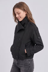 Angled front model view of a black cropped trench jacket, showing the broad collar, shoulder-tab detail, side pocket, buckled cuff and gathered hem.