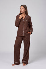 Model wearing a chocolate long sleeve pyjama set with white contrast piping, a notched-collar button-through shirt, chest pocket and matching full-length trousers.