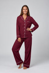 Front model view of a burgundy long sleeve pyjama set with white piping, a notched-collar button-through shirt, chest pocket and matching long trousers.