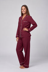 Angled front model view of a burgundy pyjama set showing the white contrast piping, chest patch pocket, long sleeve cuffs and relaxed matching trousers.