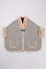 Flat product view of the beige and black textured knit poncho cape with faux fur trim, front buckle closure and two patch pockets.