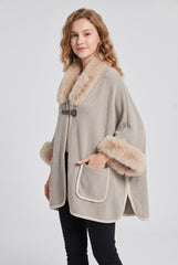 Angled model view of the beige faux fur trim winter poncho cape, showing the relaxed batwing shape, side opening and front pocket.