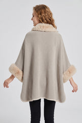 Back model view of the beige textured knit poncho cape with faux fur collar and cuffs and a loose draped silhouette.