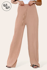 Close-up of tan plissé fabric – textured detail of pleated wide leg trousers.