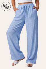 Front view of a model wearing RELA RELA Blue pinstripe relaxed-fit trousers, with an elasticated high-rise waistband, side pockets and a full-length wide-leg drape on a clean white backdrop.