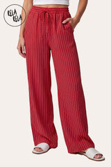 Front view of a model wearing RELA RELA Red pinstripe relaxed-fit trousers, with an elasticated high-rise waistband, side pockets and a full-length wide-leg drape on a clean white backdrop.