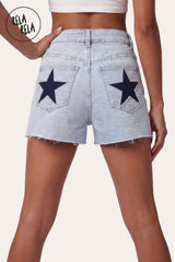 Back view of model wearing RELA RELA Royal Blue Star Diamante Light Wash Denim Shorts, featuring twin back pockets with statement royal-blue star diamante embellishments, rhinestone-trim detailing, and raw distressed hem.