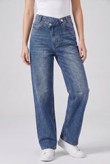 Front model view of RELA RELA Mid Wash Blue asymmetric cross-front high-waist wide-leg jeans, showing the crossover waistband, washed stretch denim and full-length leg.